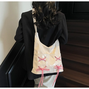 Detail of white glossy bucket bag featuring pink ribbon bow accents and wide shoulder strap