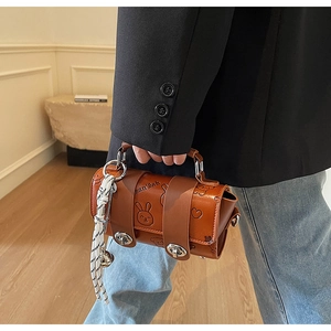 Detail of a brown cylindrical handbag with embossed cartoon patterns and hanging bell charm