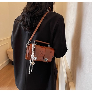 Detail of a brown cartoon leather crossbody bag with charms on a black blazer
