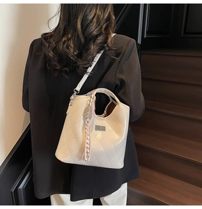 Détail d'un sac seau matelassé beige avec charme en foulard de soie et plaque argentée