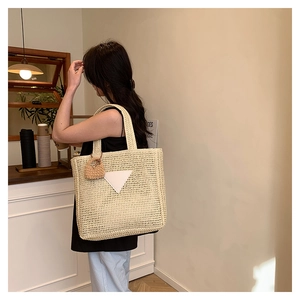Détail d'un grand sac cabas tissé beige avec pendentif cœur dans un café chaleureux
