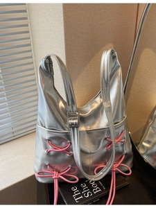 Silver metallic shoulder bag with pink bow ribbon ties and adjustable strap on display