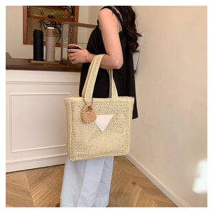 Détail du sac cabas beige tressé avec écusson triangulaire et breloque poupée mignonne