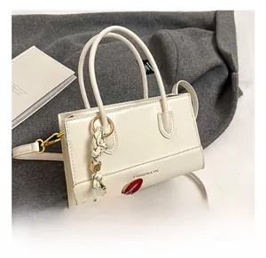 Nahaufnahme der cremefarbenen Handtasche mit Goldschrift und dekorativem Anhänger
