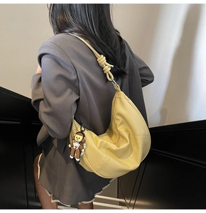 Detail of yellow soft leather hobo bag with unique knot strap and cute doll charm