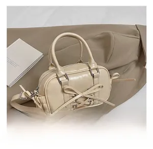 Vue détaillée du sac Boston crème avec nœud et œillets sur une veste kaki