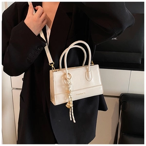 Nahaufnahme der weißen glänzenden Leder-Box-Tasche mit Glockenanhänger und Schultergurt