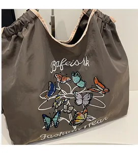 Détail de broderie papillon colorée et fermeture à cordon sur un grand sac cabas taupe