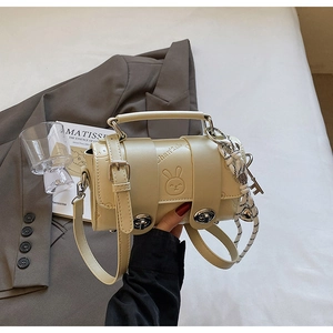 Detailed macro of cream cylinder crossbody bag with cute rabbit relief and side rope charm