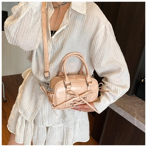 Détail d'un sac Boston rose avec nœud, texture cuir fin et bandoulière ajustable