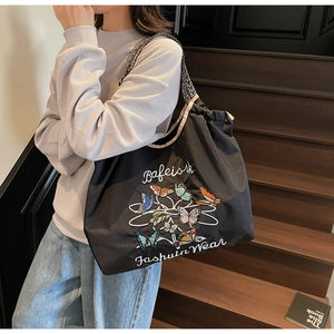 Détail d'un sac cabas en toile noire avec motif papillon et bandoulière géométrique