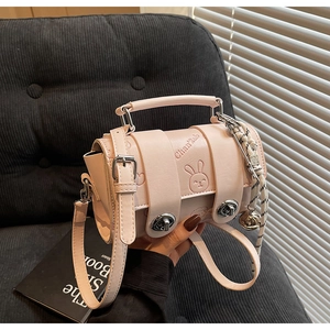 Detail of pink crossbody bag with rabbit embossment, metal turn-lock and bell charm accessory
