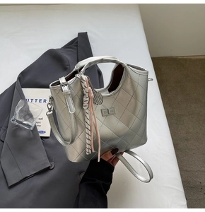 Détail d'un sac à main argenté matelassé avec fermoir rotatif et breloque à nœud décoratif