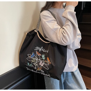 Modèle portant un grand sac cabas noir en toile avec imprimé papillon et bandoulière