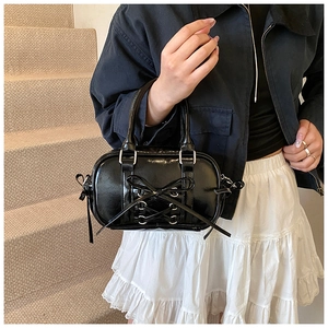 Détail du sac Boston noir brillant avec nœud papillon et œillets métalliques argentés