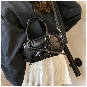 Détail d'un sac Boston noir brillant avec nœud papillon et garnitures argentées sur modèle