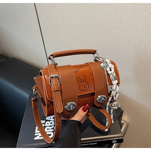 Detail view of brown mini bag with animal prints, metal knob, and woven bell charm