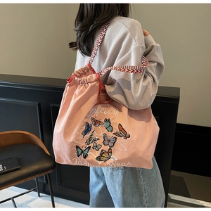 Détail du sac en toile rose avec broderies papillons colorées et anses tissées