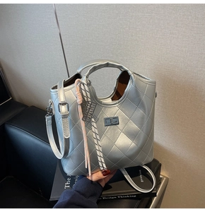 Détail du sac argenté matelassé avec fermoir rotatif en métal et pendentif tissé élégant