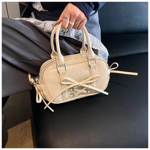 Détail du sac Boston crème avec nœud et ferrures argentées tenu par un mannequin chic
