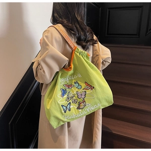 Détail d'un sac cabas vert en toile avec broderie papillon et bandoulière tissée