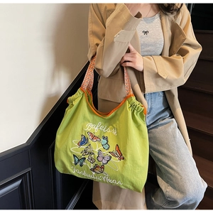 Détail du sac en toile verte avec broderie papillon et anses tissées géométriques oranges