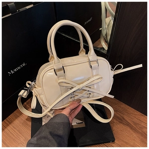 Détail du sac Boston en cuir brillant crème avec nœud décoratif et boucles argentées