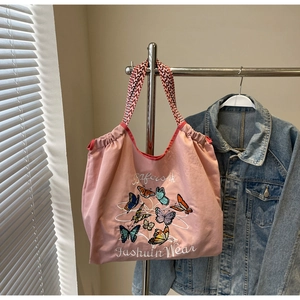 Détail d'un cabas en toile rose avec broderies papillons et anses tissées rouges
