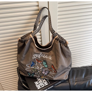 Détail de broderie papillon colorée et sangle tissée sur un sac fourre-tout taupe