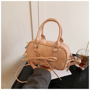 Détail du sac Boston rose abricot avec nœud ruban et garnitures argentées sur table