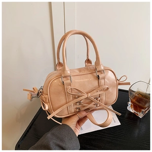 Détail du sac Boston rose avec grand nœud et sangles croisées sur une table en bois