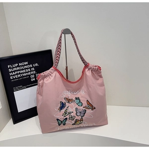 Détail de la broderie papillon et de la sangle tissée sur un sac cabas en toile rose