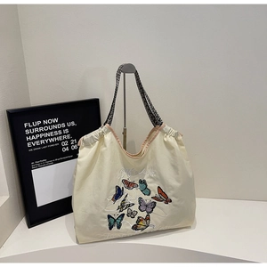 Détail de broderies papillon colorées et poignées tissées sur un sac en toile