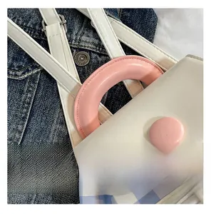 Close-up of white mini backpack with pink round handle and metal strap buckle