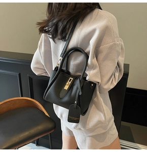 Side view of a black lychee texture bucket bag with gold metal buckle and leather tag