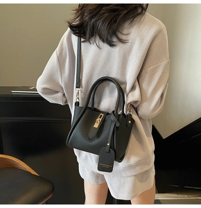 Model wearing a black pebble leather bucket bag with gold hardware and a long crossbody strap