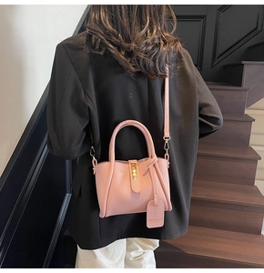 Detail of light pink pebble leather bucket bag featuring gold hardware and a luggage tag