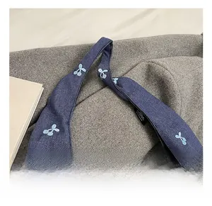 Gros plan d'un sac cabas en denim bleu avec broderie cerise et poignée solide en détail