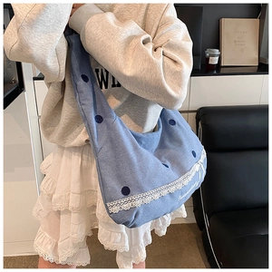 Détail du sac hobo en denim bleu avec pois foncés, bordure en dentelle et broderie