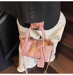 Pink lychee grain leather bucket bag with gold lock and adjustable strap held by model