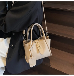 Detail of beige lychee leather bucket bag with gold lock on model in black blazer