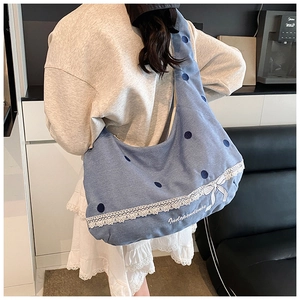 Détail du sac hobo en jean bleu avec dentelle blanche, broderie nœud et écriture