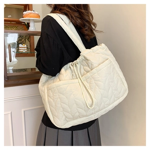Macro view of cream quilted tote bag with V-shaped stitching and front drawstring pocket
