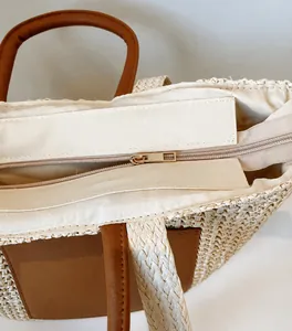 Detail eines glatten Gold-Reißverschlusses an einer gewebten Strohtasche mit Ledergriff
