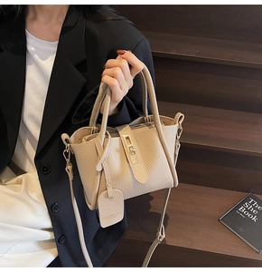 Detail of beige lychee leather bucket bag featuring gold metal buckle and hanging brand tag