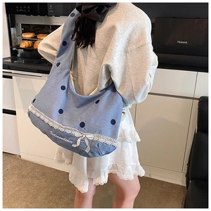 Détail du sac hobo en denim bleu avec dentelle blanche, nœud et motif à pois