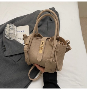 Detail of khaki pebbled leather bucket bag featuring a gold twist lock and a long strap