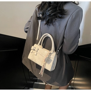Dettaglio di un'elegante borsa a mano crema con fiocco e ciondolo indossata su un blazer