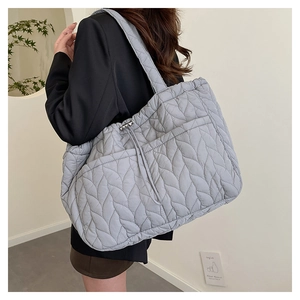 Detail of grey quilted tote bag with leaf pattern and adjustable drawstring side on model