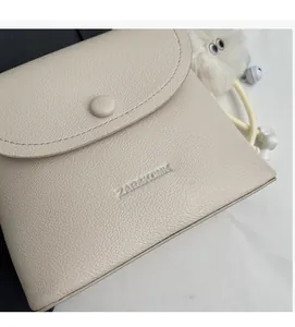 Detail shot of beige pebbled leather texture and embossed ZAR&KCMK logo on crossbody bag